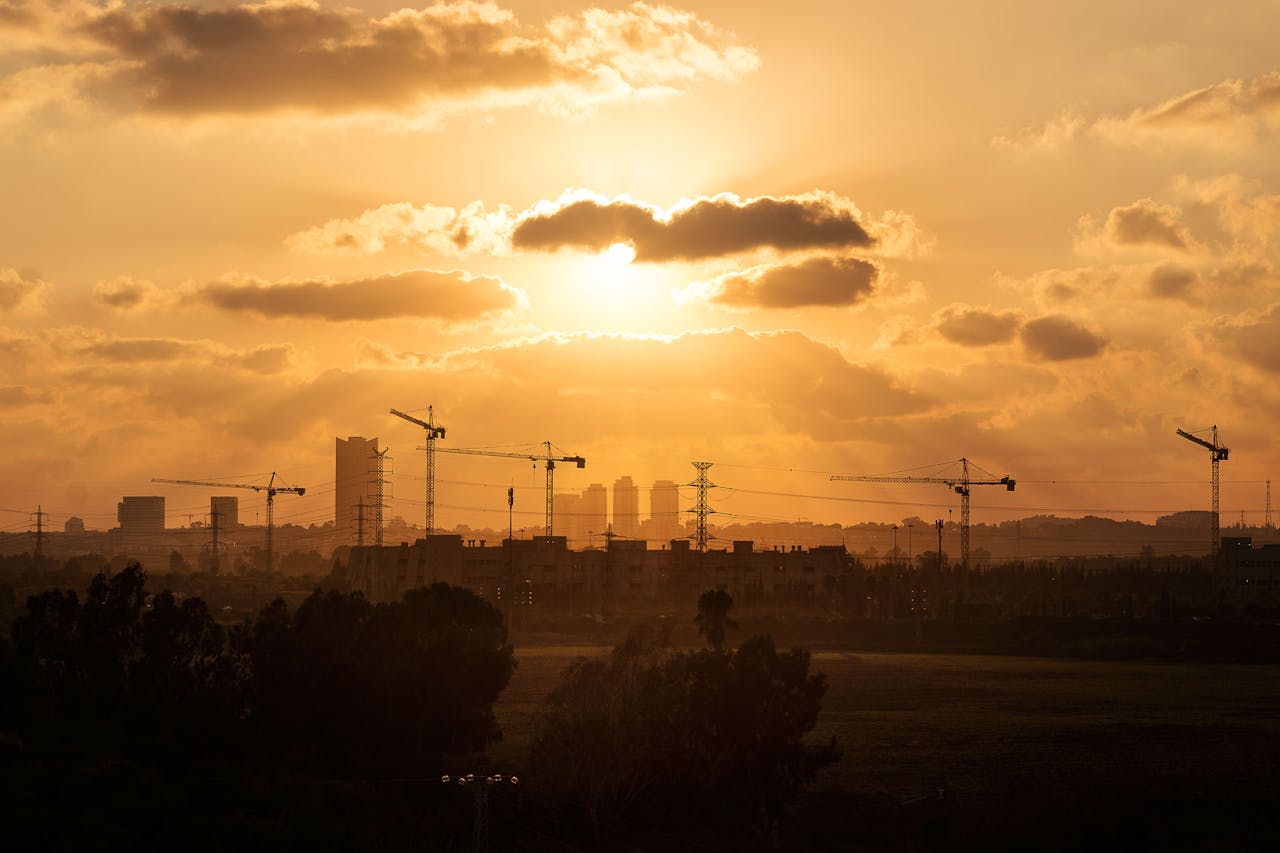 City skyline with construction cranes silhouetted against a sunset sky.